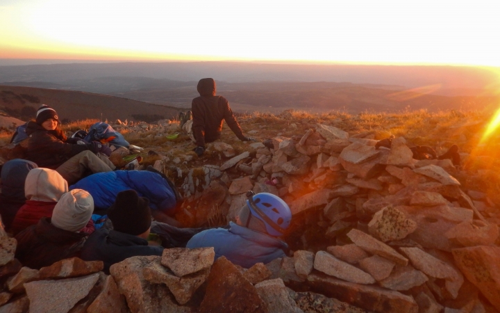 A group of people huddle at their campsite as the sunrises
